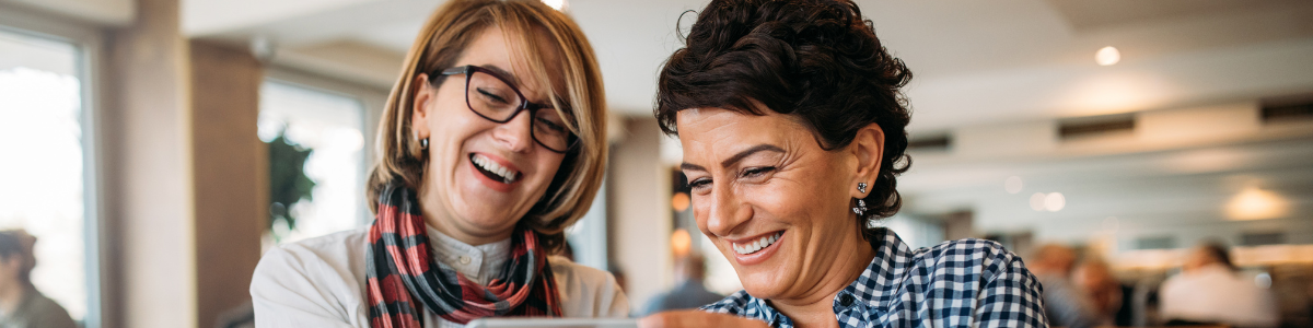 two middle aged women laughing and smiling while on a tablet